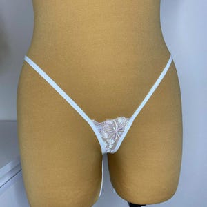 Puede incluir: Lingerie de encaje blanco con un dise&ntilde;o floral. La lencer&iacute;a tiene tirantes finos y una tela delicada y transparente.