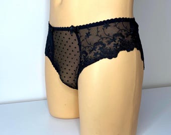 Könnte beinhalten: Schwarze Unterwäsche mit einem transparenten Punktmuster auf der Vorderseite und floraler Spitzenborte. Die zarte Dessous-Wäsche hat eine kleine Schleife an der Taille und einen gewellten Saum. Das Kleidungsstück wird auf einer Schaufenquinpuppe präsentiert.