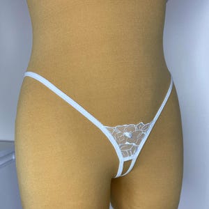 May include: White lace lingerie with a floral design. The lingerie has a thin strap that goes around the waist and ties at the front.