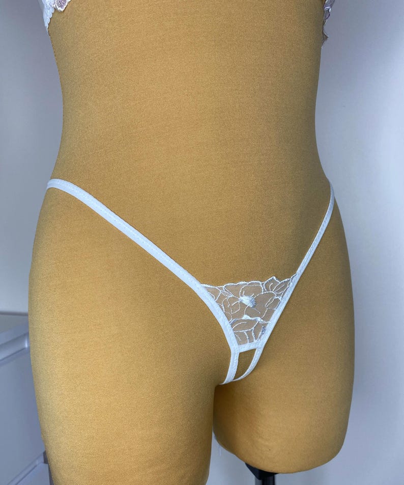 May include: White lace lingerie with a floral design. The lingerie has a thin strap that goes around the waist and ties at the front.