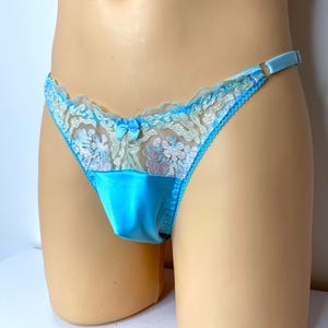 Può includere: Perizoma azzurro chiaro con pannello frontale in raso e delicati dettagli in pizzo. Il pizzo presenta un motivo floreale con sfumature di rosa e blu. Un piccolo fiocco adorna la parte anteriore, aggiungendo un tocco di eleganza alla lingerie.