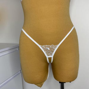 May include: White lace lingerie with a delicate floral pattern. The lingerie has a low-rise cut and thin straps.