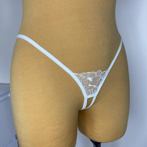 May include: White lace lingerie with a floral design. The lingerie has a low rise and a small opening in the front.