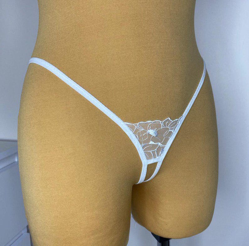 May include: White lace lingerie with a floral design. The lingerie has a low rise and a small opening in the front.