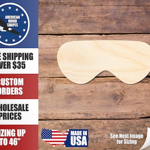 Puede incluir: Un recorte de madera de una máscara para dormir, con forma de un par de ojos. El recorte está hecho de madera sin terminar y está listo para ser pintado o teñido. El recorte se muestra sobre un fondo de madera.