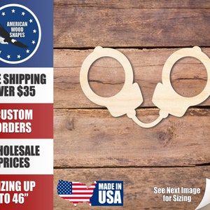 May include: Wooden cutout of a pair of handcuffs. The cutout is made of light brown wood and is on a brown wood background. The cutout is approximately 6 inches in size.