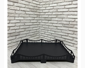 Puede incluir: Bandeja de servir de metal negro con un borde ondulado decorativo. La bandeja tiene una superficie negra plana y se apoya en cuatro patas cortas.