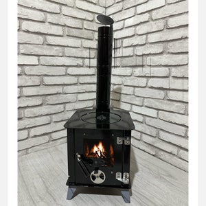 May include: A black wood-burning stove with a glass door and a metal chimney. The stove is sitting on a wooden floor in front of a white brick wall. The stove is lit and there is a fire burning inside.