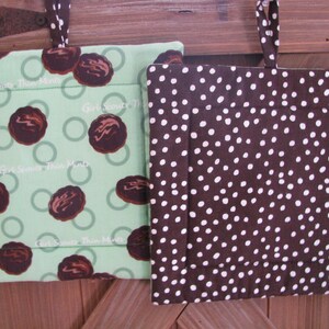 May include: Two square quilted pot holders with fabric hanging loops. One features a light green background with a repeating pattern of brown chocolate cookies and the text Girl Scouts Thin Mints. The other is dark brown with white polka dots.