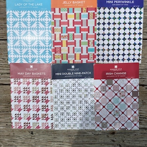 May include: Six Missouri Star Quilt Co. pattern booklets featuring Lady of the Lake, Jelly Basket, Mini Periwinkle, May Day Baskets, Mini Double Nine-Patch, and Irish Change. Each rectangular booklet displays a colorful quilt design on the cover.