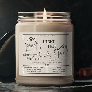 May include: A beige soy wax candle in a clear glass jar with a black lid. The label reads "Light This When You Miss Me" with house numbers 07459 and 32816. The candle is 9 oz and is completely natural, vegan, and non-toxic.