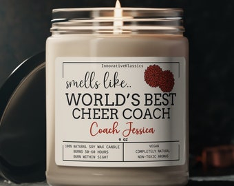 May include: A brown soy wax candle with a white label that reads "smells like... WORLD'S BEST CHEER COACH Coach Jessica 9 oz 100% NATURAL SOY WAX CANDLE BURNS 50-60 HOURS BURN WITHIN SIGHT VEGAN COMPLETELY NATURAL NON-TOXIC AROMAS".