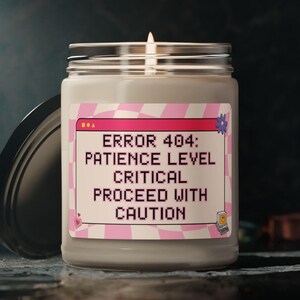 May include: A white candle with a pink and white label that reads "ERROR 404: PATIENCE LEVEL CRITICAL PROCEED WITH CAUTION".