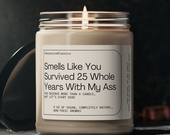 May include: A beige candle with a glass jar and a black lid. The candle has a white label with the text "Smells Like You Survived 25 Whole Years With My Ass" and the text "9 oz of vegan, completely natural, non-toxic aromas".