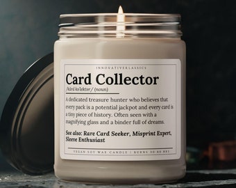 Può includere: Una candela accesa in cera di soia in un barattolo di vetro con coperchio argentato. L'etichetta recita "Card Collector" con una definizione e termini correlati. La candela è su una superficie scura e strutturata.