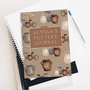 May include: A brown journal with a pattern of watercolor illustrations of pottery. The text "ALYSSA'S POTTERY JOURNAL" is printed on the front cover.