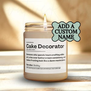 May include: A lit candle in a glass jar with a label that reads "Cake Decorator." The label includes a definition and the words "Add a Custom Name." The candle burns for 50-60 hours.