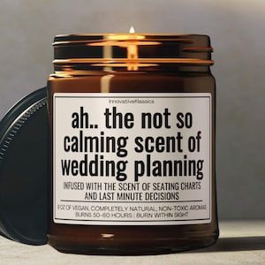 May include: A brown glass candle jar with a black lid. The candle is labeled "ah... the not so calming scent of wedding planning". The label also says "Infused with the scent of seating charts and last minute decisions".