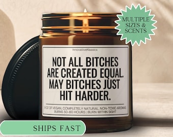 May include: A brown glass jar candle with a black lid, featuring the text "NOT ALL BITCHES ARE CREATED EQUAL. MAY BITCHES JUST HIT HARDER." The label also states the candle is vegan and burns for 50-60 hours. A green banner reads "SHIPS FAST."