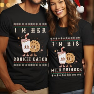 Puede incluir: Una pareja lleva suéteres navideños negros a juego con un diseño de cartón de leche y galletas. El suéter de la izquierda dice "Soy su comedor de galletas" y el suéter de la derecha dice "Soy su bebedor de leche".