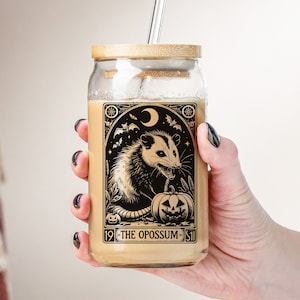 May include: A glass mason jar with a bamboo lid and a straw. The jar has a black and white illustration of an opossum with a pumpkin and the text "19 - THE OPOSSUM - 51".