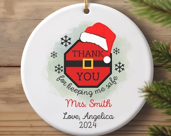 May include: White ceramic Christmas ornament with a red and white Santa Claus design. The ornament says "Thank You for keeping me safe" and "Mrs. Smith Love, Angelica 2024".