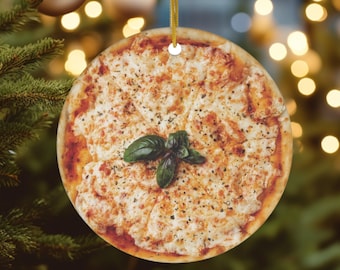 May include: A round ceramic ornament featuring a pizza with melted cheese, tomato sauce, and a sprig of basil. The ornament has a gold string for hanging.