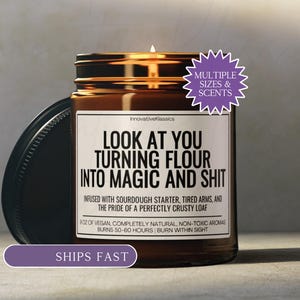 May include: A lit brown glass jar candle with a black lid. The candle has a white label with the text "LOOK AT YOU TURNING FLOUR INTO MAGIC AND SHIT". The candle is infused with sourdough starter and burns for 50-60 hours.