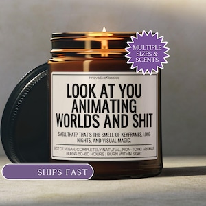 May include: A lit brown glass jar candle with a black lid. The candle has a white label with black text that reads "LOOK AT YOU ANIMATING WORLDS AND SHIT". The candle is 9 oz and burns for 50-60 hours.