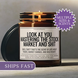 May include: A lit brown glass candle jar with a black lid. The label reads "LOOK AT YOU MASTERING THE STOCK MARKET AND SHIT." The candle is 9 oz and burns for 50-60 hours. The text "MULTIPLE SIZES & SCENTS" is also visible.