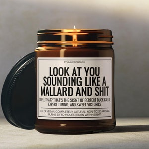 Pu&ograve; includere: Una candela accesa in un barattolo di vetro marrone con coperchio nero. La candela ha un'etichetta bianca con testo nero che dice "LOOK AT YOU SOUNDING LIKE A MALLARD AND SHIT". La candela &egrave; di 255 grammi e brucia per 50-60 ore.