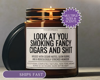 May include: A brown glass candle jar with a black lid and a white label featuring the text: LOOK AT YOU SMOKING FANCY CIGARS AND SHIT. INFUSED WITH CEDAR NOTES, SLOW BURNS, AND A RIDICULOUSLY STOCKED HUMIDOR. 9 OZ OF VEGAN, COMPLETELY NATURAL, NON-TOXIC AROMAS.