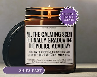 May include: A lit brown glass jar candle with a black lid. The label reads "AH.. THE CALMING SCENT OF FINALLY GRADUATING THE POLICE ACADEMY." The candle is labeled "Multiple Sizes & Scents" and is described as vegan and non-toxic.