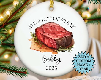 May include: White ceramic Christmas ornament with a gold string. The ornament features a watercolor illustration of a steak with the text "ATE A LOT OF STEAK" above it. Below the steak is the name "Bobby" and the year "2025".