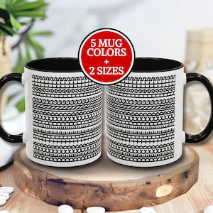 May include: Two white coffee mugs with black handles and rims, featuring a black and white geometric pattern. A red circle with the text "5 MUG COLORS + 2 SIZES" is visible. The mugs are displayed on a wooden surface.