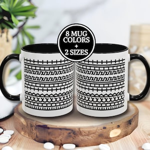 May include: Two white ceramic mugs with black handles and rims, featuring a black and white geometric pattern. The mugs are displayed on a wooden surface. A circular graphic states "8 MUG COLORS + 2 SIZES".