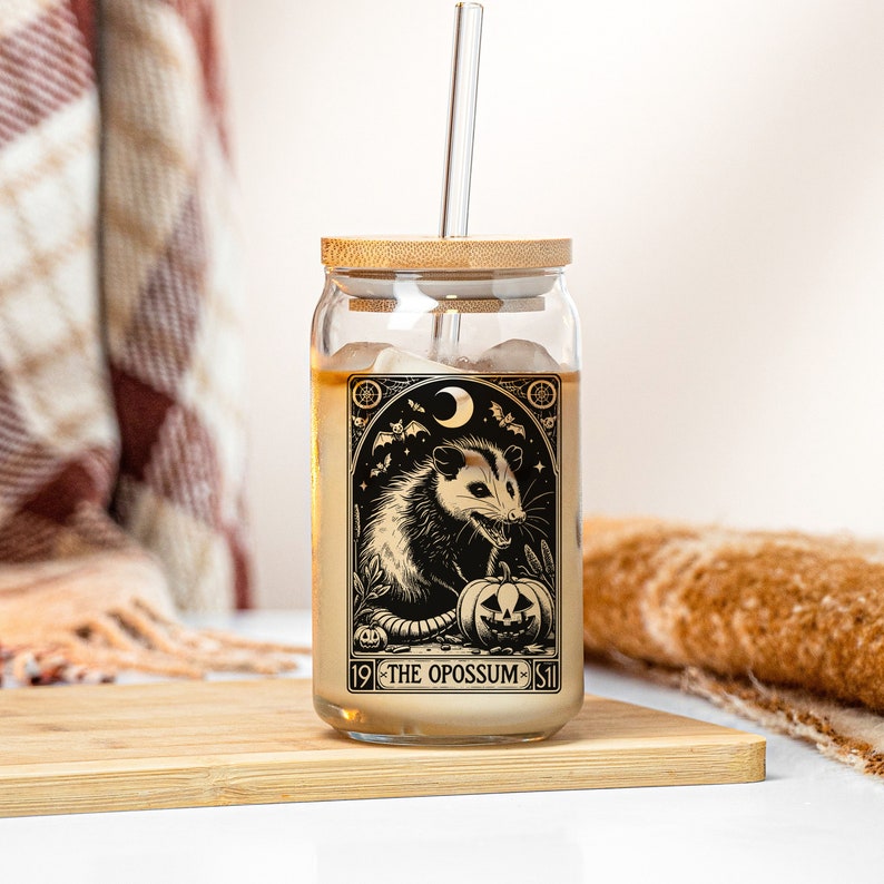 May include: A glass jar with a bamboo lid and a straw. The jar has a black and white illustration of an opossum with a pumpkin. The text on the jar reads "19 THE OPOSSUM 51".