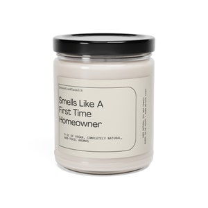 May include: A glass jar candle with a black lid. The label reads "Smells Like A First Time Homeowner" and "9 oz of Vegan, Completely Natural, Non-Toxic Aromas".