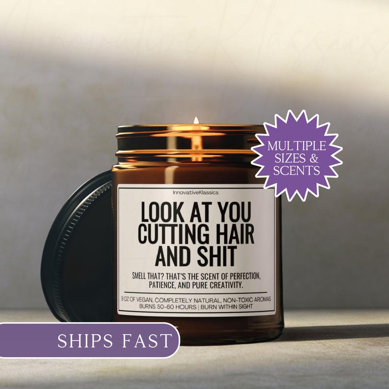 Puede incluir: Una vela en tarro de cristal marr&oacute;n con tapa negra. La vela tiene una etiqueta blanca con el texto "LOOK AT YOU CUTTING HAIR AND SHIT". La vela est&aacute; etiquetada como "InnovativeKlassics" y tiene un tiempo de combusti&oacute;n de 50-60 horas. La vela est&aacute; etiquetada "Multiple Sizes & Scents".