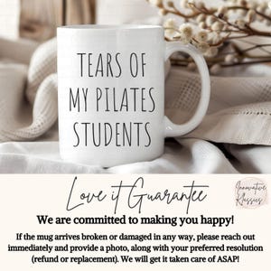 May include: White ceramic coffee mug with black text that reads "Tears of My Pilates Students". The mug is sitting on a white and beige fabric surface.