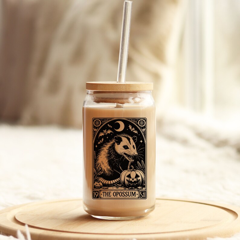 May include: A glass jar with a wooden lid and a straw. The jar has a black and white illustration of an opossum holding a jack-o-lantern. The text on the jar reads "19 - THE OPOSSUM - 11".