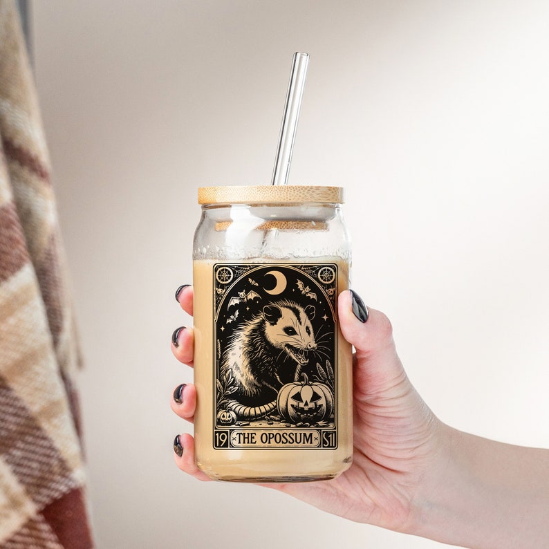 May include: A glass mason jar with a bamboo lid and a straw. The jar has a black and white illustration of an opossum with a pumpkin and the text "19 - THE OPOSSUM - 51".