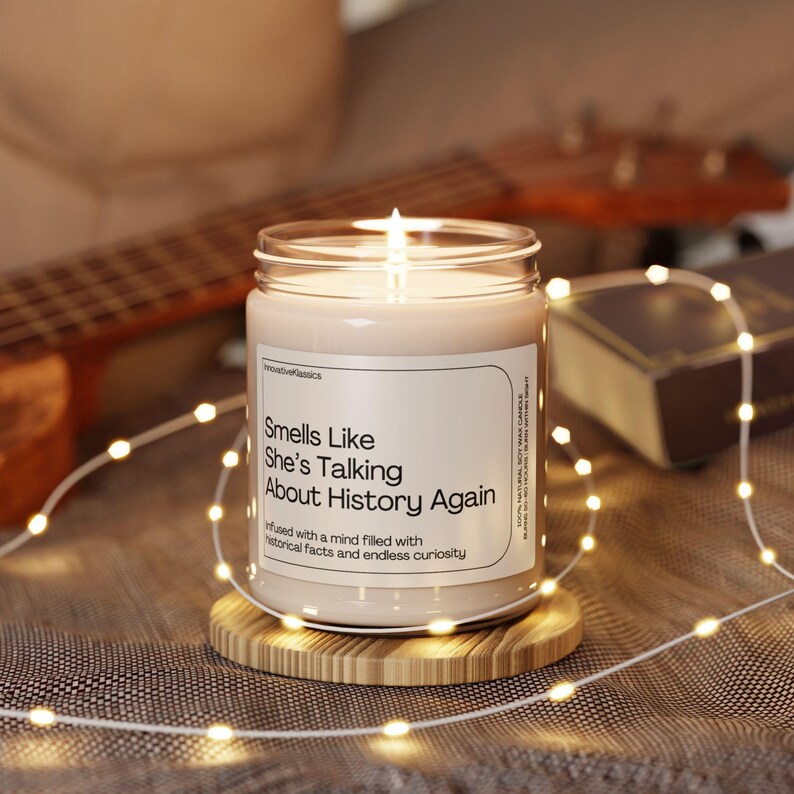 May include: A candle in a glass jar with a white label that reads "Smells Like She's Talking About History Again" and "infused with a mind filled with historical facts and endless curiosity".