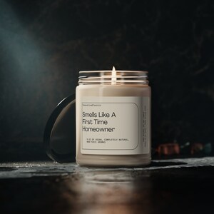 May include: A beige candle in a glass jar with a black lid. The candle is labeled "Smells Like A First Time Homeowner" and "9 oz of Vegan, Completely Natural, Non-Toxic Aromas".