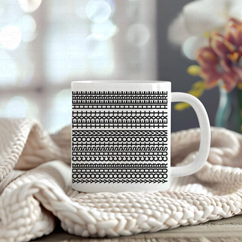 Pu&ograve; includere: Tazza in ceramica bianca con un motivo nero ripetuto di forme geometriche. La tazza ha un manico curvo ed &egrave; appoggiata su una coperta di maglia color crema. Lo sfondo &egrave; sfocato, con accenni di fiori.