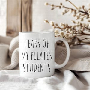 May include: White ceramic mug with black text that reads "Tears of my Pilates Students".