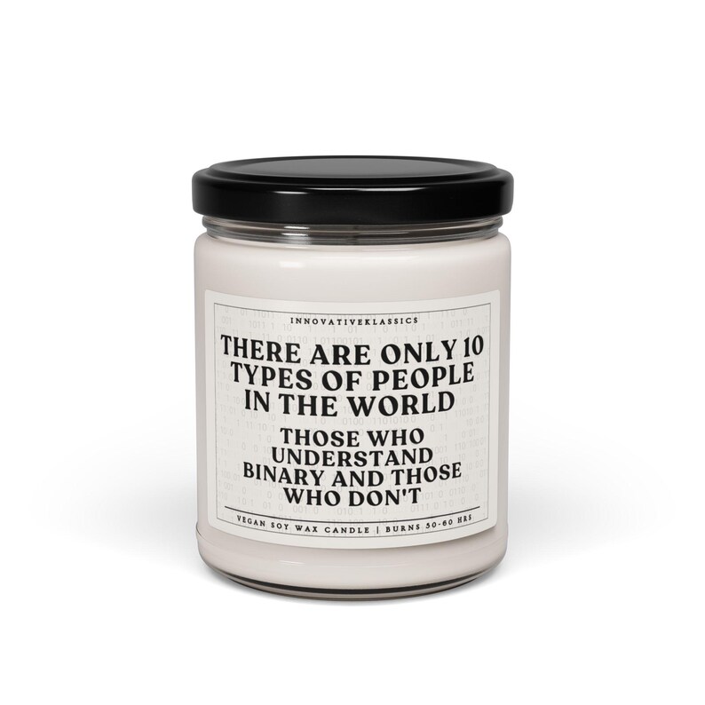 May include: A white soy wax candle with a black lid. The candle has a quote printed on the front: "There are only 10 types of people in the world. Those who understand binary and those who don't." The candle is vegan and burns for 50-60 hours.