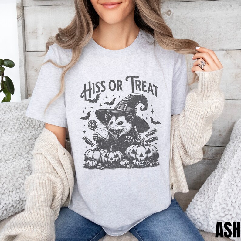 May include: A gray t-shirt with a black and white illustration of a possum wearing a witch hat and holding a lollipop. The text "Hiss or Treat" is printed above the possum.