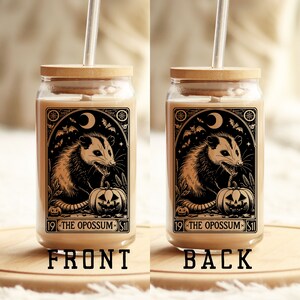 May include: A glass jar with a wooden lid and a straw. The jar has a black and white illustration of an opossum with a pumpkin and bats. The text on the jar reads "19 - THE OPOSSUM - 51".