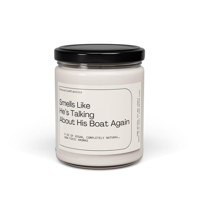 Op de afbeelding: Een witte kaars pot met een zwarte deksel. Het etiket luidt "Smells Like He's Talking About His Boat Again". De kaars is 9 oz vegan, volledig natuurlijk, niet-toxische aroma's.